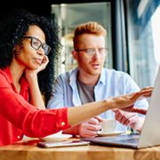 Businesswoman in glasses pointing finger on laptop screen and discussing work with colleague